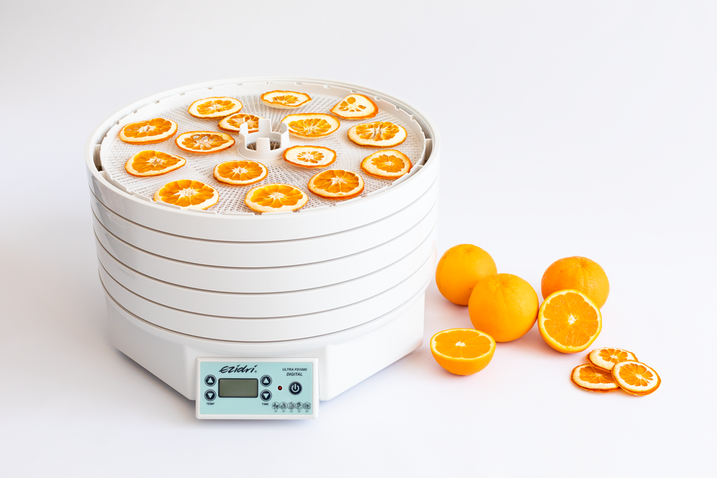 Dried orange slices on the top tray of an Ezidri Ultra FD1000 dehydrator, with fresh oranges beside it